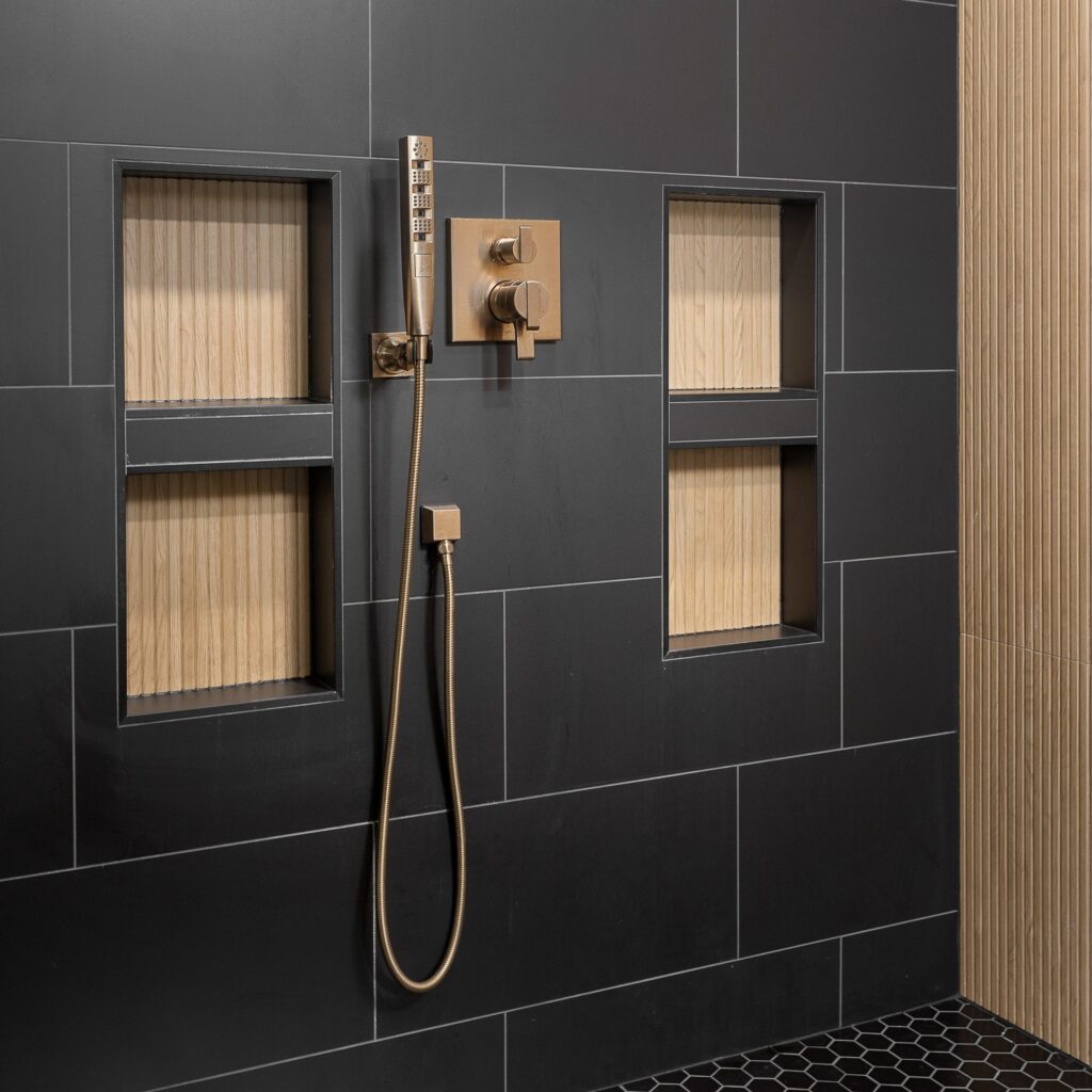 Walk-in shower with charcoal tile, bronze fixtures and wood-slat niches
