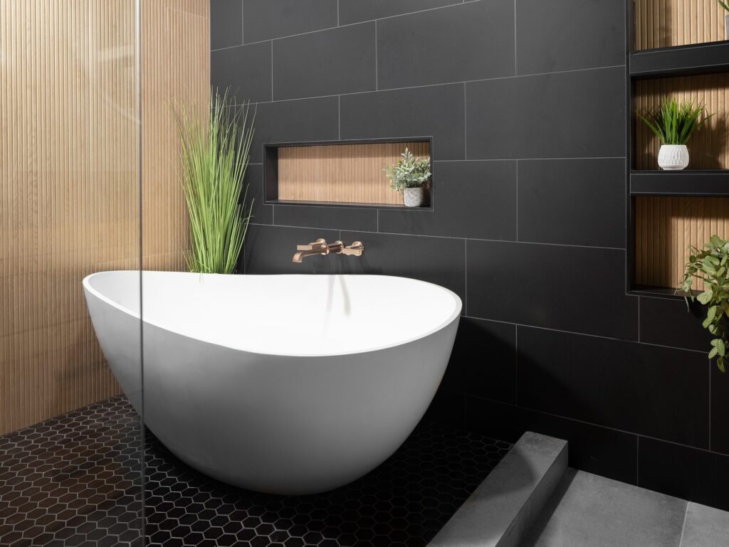 Freestanding soaking tub with brushed bronze wall faucet and wood-slat niche